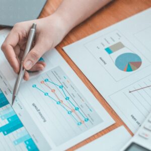 Mani che annotano dati su documenti con grafici, su un tavolo.