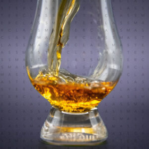 Bicchiere da degustazione con liquore ambrato in versamento su sfondo scuro
